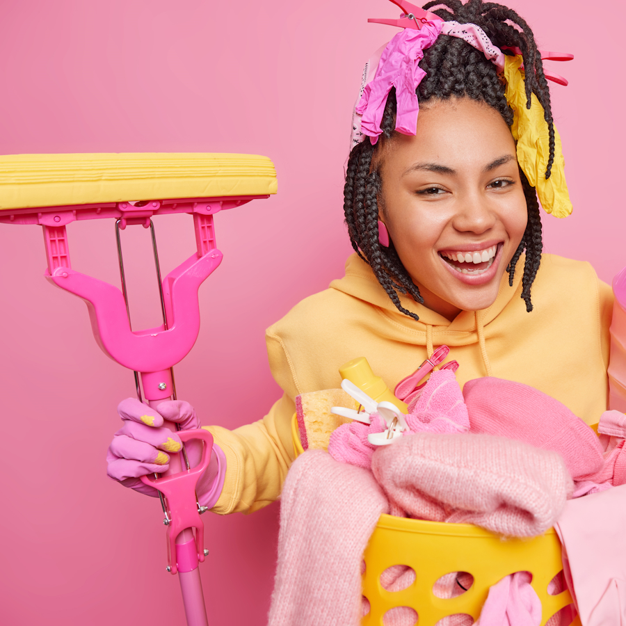 Woman smiling while holding a mop in on hand and a bucket of cleaning supplies in the other