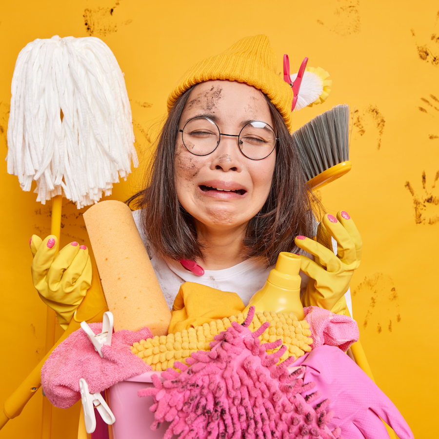 Woman covered in dust and looking sad while surrounded by cleaning supplies used for dusting